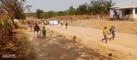 Cortège d'élèves et de jeunes marchant sur une route de terre à Koui lors d'une manifestation forcée en faveur du troisième mandat de Touadéra