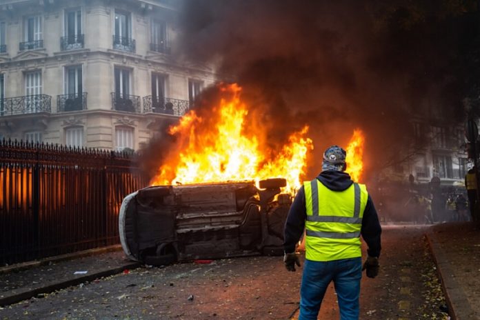 Un gilet jaune devant une voiture incendiée à Paris. un-gilet-jaune-devant-une-voiture-incendiee-paris-1 CENTRAFRIQUE/FRANCE : GILETS JAUNES,  INQUIÉTUDE A BANGUI, SATISFACTION A MOSCOU