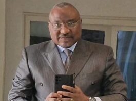 Monsieur Marcel Djimassé, ministre de la Fonction publique de Centrafrique habillé en costume devant son téléphone portable. Il porte ses verres progressives