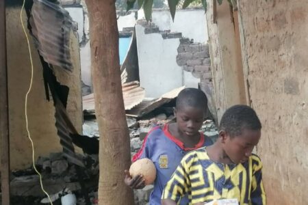 Deux adolescents curieux de même âge, un en chemise jaune et l’autre, dernier lui en chemise bleue tenant un ballon de foot à la main, entrain de marcher sur les gravats de la maison incendiée au quartiers Castors à Bangui 