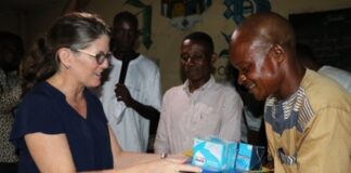 Remise de fournitures scolaires par Bridget Premont, chef de mission adjointe de l’ambassade des États-Unis à Bangui au directeur de l’école de Bobangui, souriant dans une salle de classe avec des spectateurs en arrière-plan.