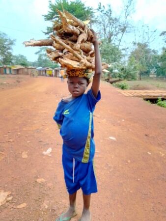 Enfant portant un panier de tubercules de manioc sur la tête sur une route de terre rurale à Boda, à l’ouest de la République centrafricaine.