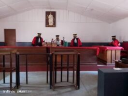 Vue intérieure d’un tribunal avec des juges en tenue officielle assis derrière le banc des magistrats, entourés de mobilier en bois.