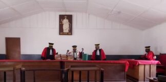Vue intérieure d’un tribunal avec des juges en tenue officielle assis derrière le banc des magistrats, entourés de mobilier en bois.