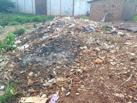 Route de terre bordée de débris et d’ordures près d’habitations, signe d’un manque de gestion des déchets