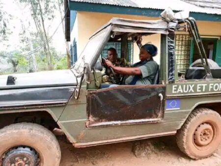 Deux agents des eaux et forêts discutant dans un véhicule tout-terrain boueux marqué de l’insigne de l’Union Européenne dans une zone forestière.
