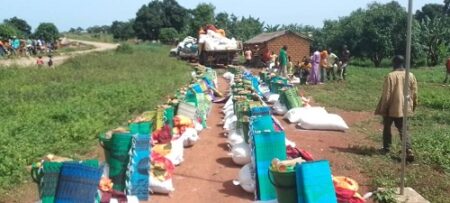 Distribution de kits de secours aux personnes déplacées à Koundé, montrant des sacs de vivres et des kits divers alignés sur le sol, prêts à être distribués.