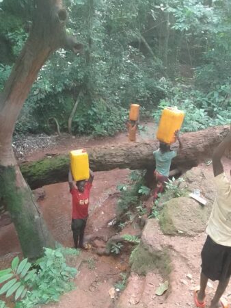 Des enfants du village de Yangoubanda transportant des jerrycans d’eau sur leurs têtes, traversant une forêt.