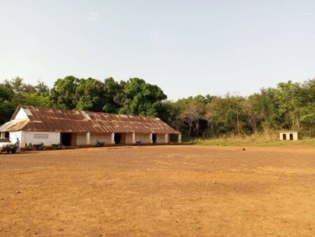 Image d’une grande école rurale à toit de tôle à Yalinga, avec un large terrain dégagé devant.
