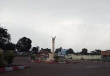 Image du rond-point principal de Bambari avec une colonne surmontée d’une sculpture d’un oiseau, au crépuscule, sous un ciel nuageux.
