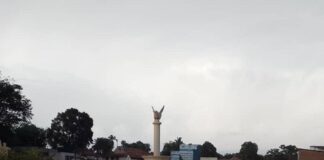 Image du rond-point principal de Bambari avec une colonne surmontée d’une sculpture d’un oiseau, au crépuscule, sous un ciel nuageux.