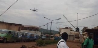 Un hélicoptère de Wagner survolant la ville de Bangui à basse altitude, avec des habitants observant depuis le sol.