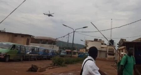 Un hélicoptère de Wagner survolant la ville de Bangui à basse altitude, avec des habitants observant depuis le sol.