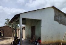 Maison en ciment avec véranda dans le village Bangarrem, avec des personnes assises à l’ombre