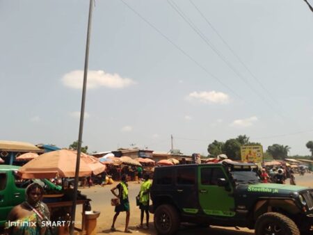Vue d’une rue animée à l’entrée du marché Gobongo, à la sortie nord de Bangui, avec des véhicules, des piétons et des vendeurs ambulants.