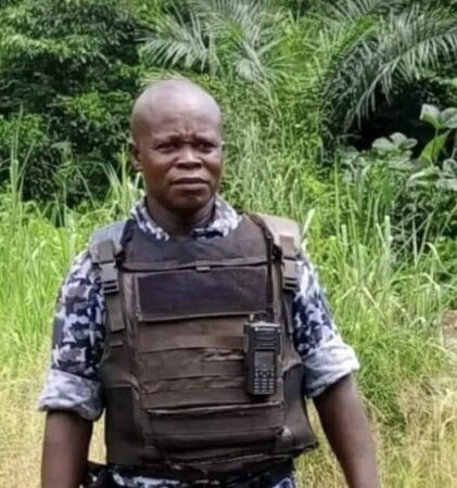 Fabrice Assap, directeur de la Compagnie Nationale de Sécurité, en tenue de patrouille, portant un gilet pare-balles et une radio, dans un environnement de végétation dense.