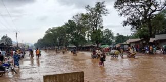 Rue inondée au marché combattant de Bangui avec des piétons et des véhicules naviguant dans l’eau boueuse.