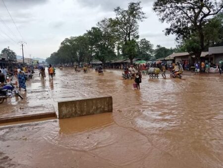 Rue inondée au marché combattant de Bangui avec des piétons et des véhicules naviguant dans l’eau boueuse.