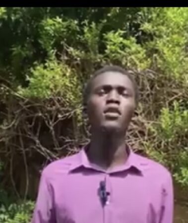 Jeune homme en chemise rose s’exprimant devant un micro en extérieur