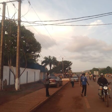 Route entre Combattant et Marabéna à Bangui avec des passants, motocyclistes, et voitures en fin d’après-midi.
