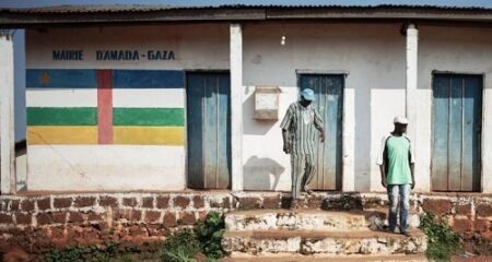 Façade de la mairie d'Amada-Gaza en République centrafricaine, avec deux hommes debout devant le bâtiment peint aux couleurs du drapeau national