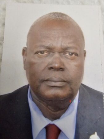 Portrait de Prosper N'douba, homme d'âge mûr à la peau noire, cheveux gris courts, portant un costume sombre avec une cravate rouge