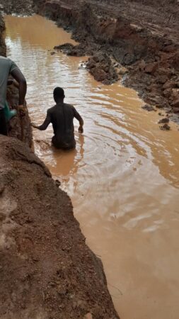 Des hommes tentent de traverser une route inondée et dégradée en direction de Paoua, démontrant les difficultés de déplacement pendant la saison des pluies.