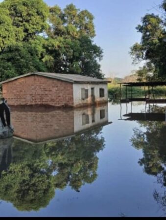 Maison en briques partiellement submergée par les inondations à Kaga-Bandoro, avec le reflet des arbres sur l'eau stagnante, illustrant l'article sur la ville de Kaga-Bandoro : L'inaction criminelle répétée du gouvernement face aux catastrophes naturelles….