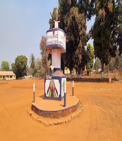 Monument de la paix à Bria, en pleine centre-de la capitale de la Haute-Kotto, République centrafricaine, entouré de terre rouge et de végétation, portant des inscriptions et des symboles nationaux.