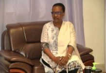 Le cancer peut-il être transmis par un simple contact ? Alors, qui a peur de qui ? Touadéra et Valentine Rugwabiza : le mystère du flacon de gel au Palais de la renaissance Madame Valentine Rugwabiza, représentante du Secrétaire général des nations-unies en Centrafrique, assise sur un canapé en cuir marron au palais de la renaissance en face du Président Touadera, avec un châle clair sur l’épaule. Elle porte des lunettes et une tunique blanche ornée de motifs floraux gris et noirs. Elle a les mains croisées sur les genoux et regarde légèrement sur le côté. À droite, on peut regarder aisément une bouteille de gel désinfectant vert sur une table.