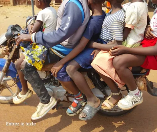 Un moto taximan avec ses clients, des élèves et adolescents, sur la route de Bangui